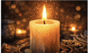 A lit pillar candle glows warmly as tiny sparks or glittering particles drift around it, with soft golden bokeh lights in the background.